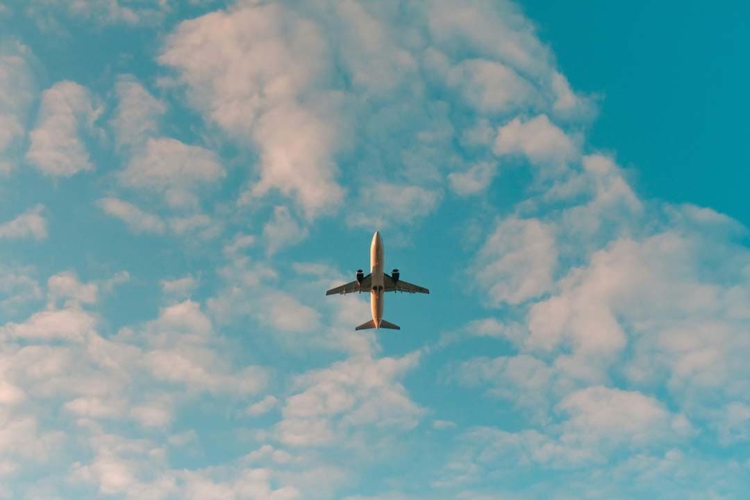 Avion survolant un ciel bleu nuageux, symbole d'évasion et de lâcher-prise. L'esprit Moody CBD : ralentir, voyager léger, retrouver son équilibre